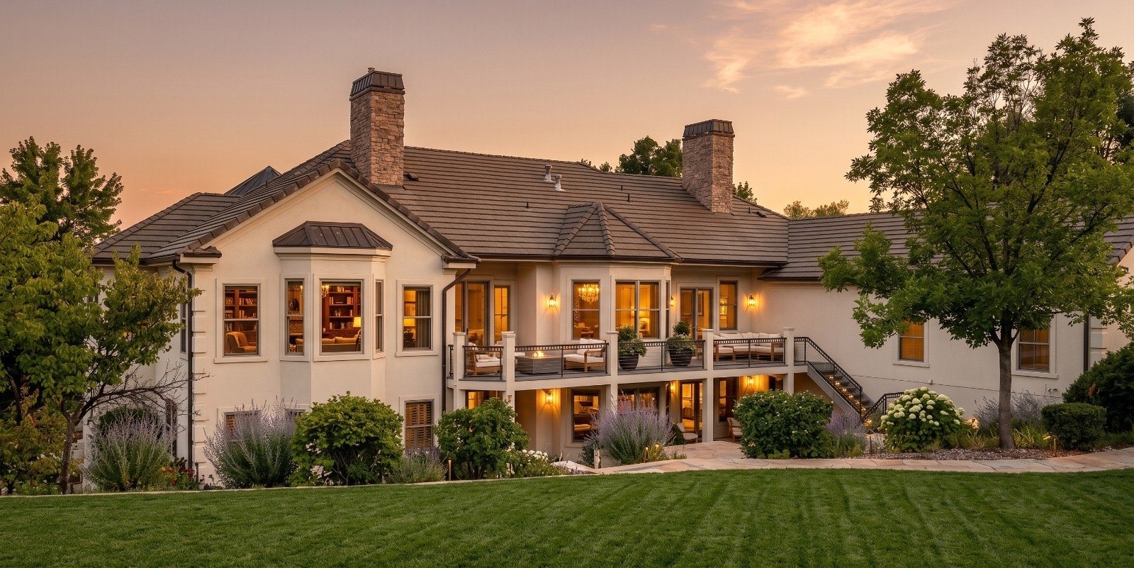 The back of the estate at sunset, with a lit deck above a wide lawn